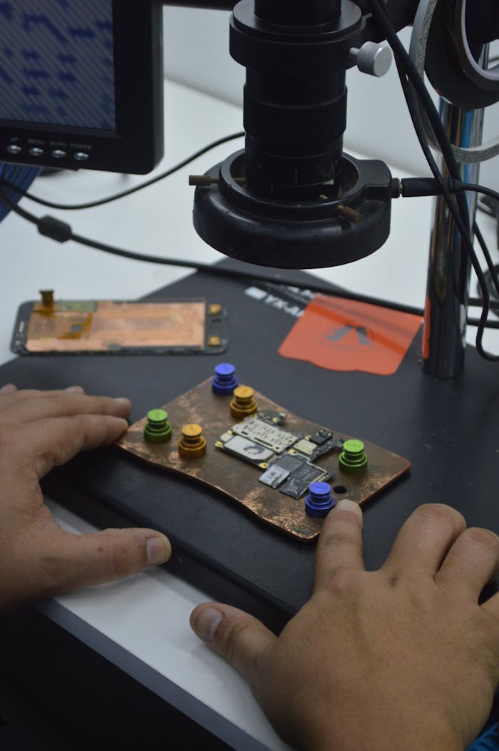 Close-up of hands working on a circuit board under a microscope in a tech lab.